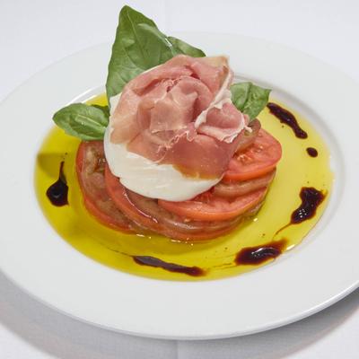 Burrata cheese on a bed of tomatoes topped with prosciutto and fresh basil.