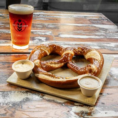 Salted pretzel with cheese dip, mustard, and a glass of beer.