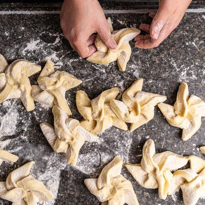 Hands shaping dough into pinwheel pastries on a floured, dark countertop.