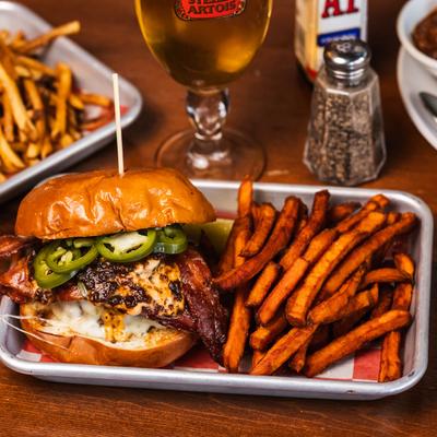 Chipotle jam burger with sweet potato fries, accompanied with a glass of beer.