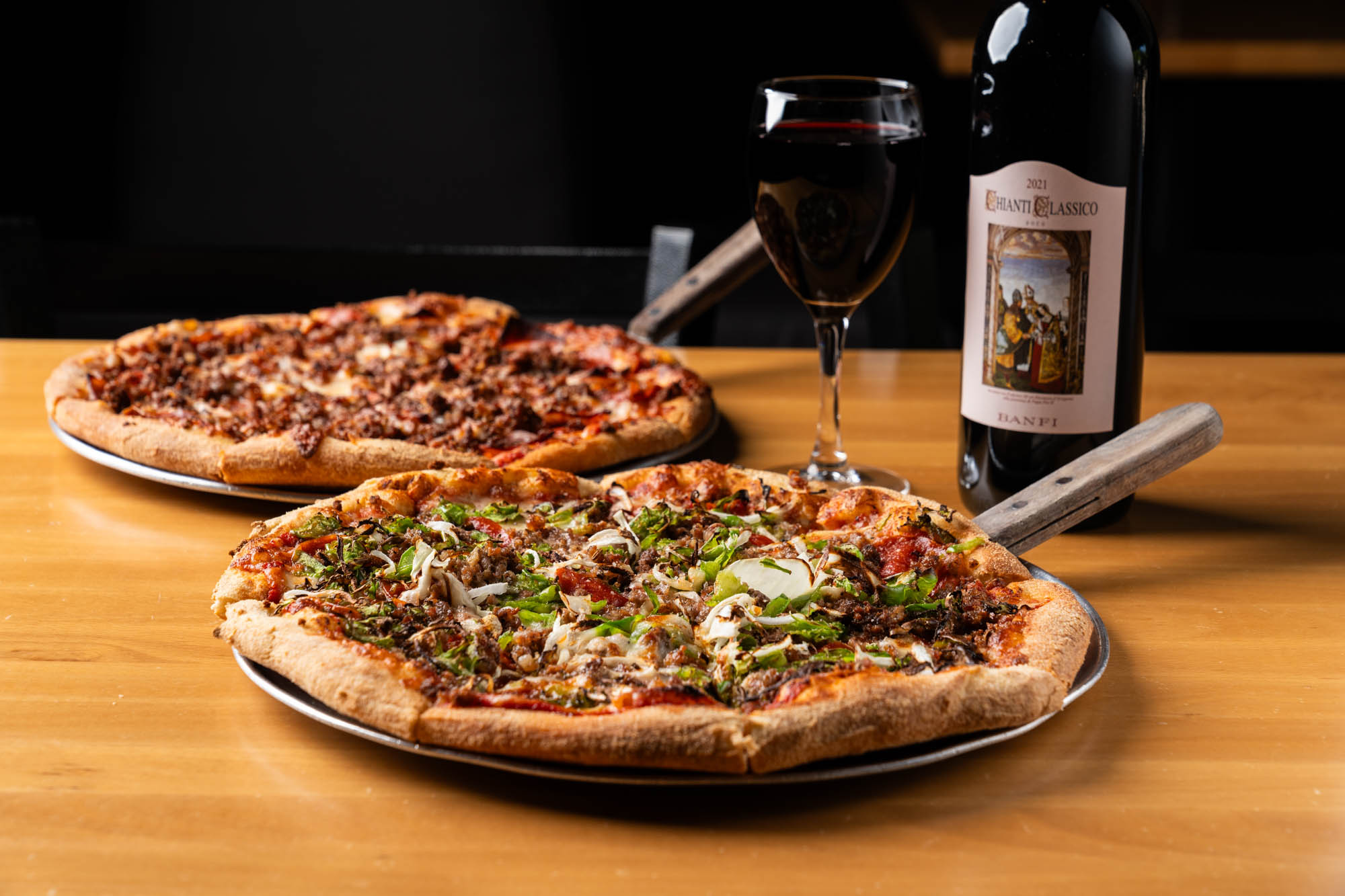 Two pizzas and wine displayed on a wooden table