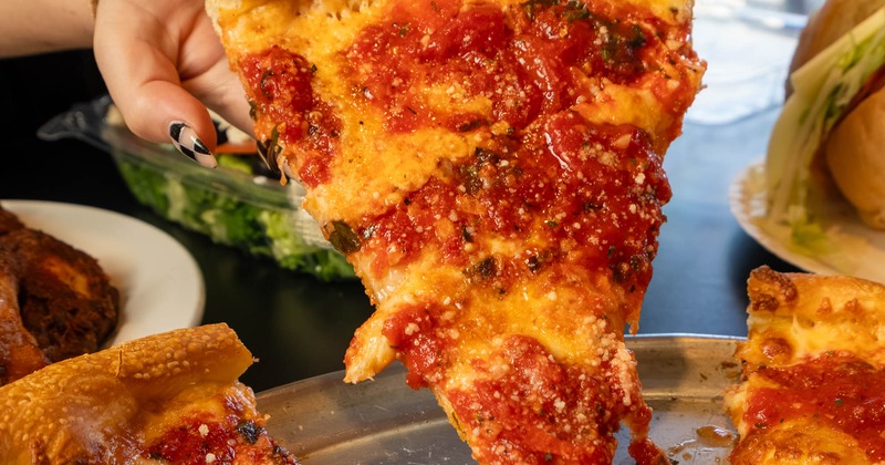 Slice of pizza being pulled from the metal tray