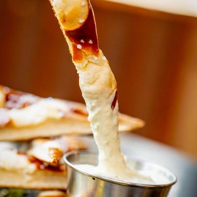 A pretzel being dipped into a cup with creamy sauce.
