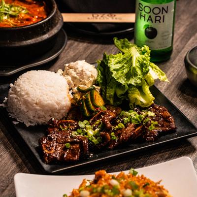 Korean galbi short ribs served with rice, lettuce, and flavored soju bottle.