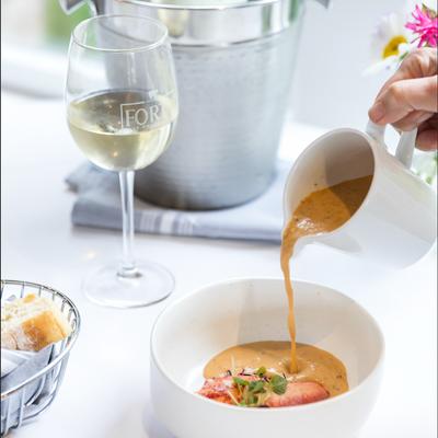 Server pouring lobster bisque into a bowl beside a glass of chilled white wine.