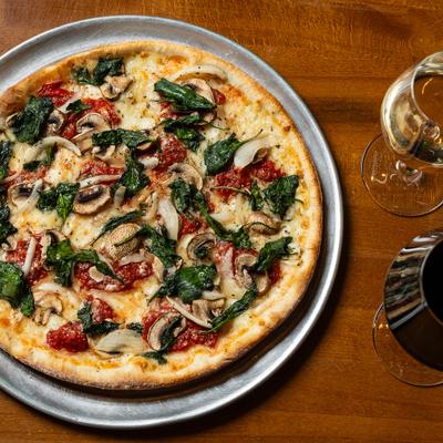 Vegetarian pizza topped with spinach, mushrooms and tomatoes, servd with wine.