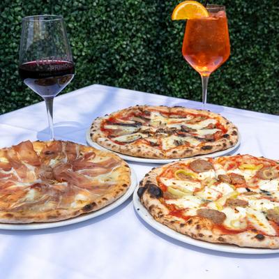 Three whole pizzas served on the table with a glass of wine and Aperol Spritz.