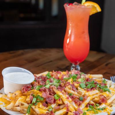 Loaded fries with bacon, scallions, and cheese, served with a Hurricane cocktail.
