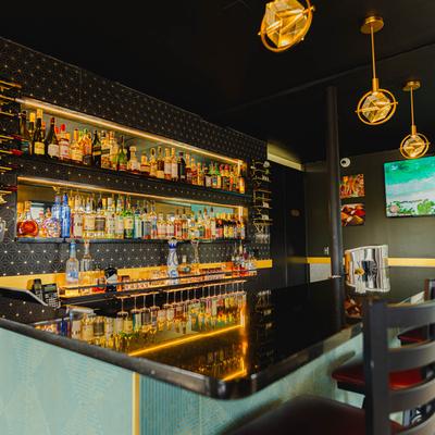 Modern bar interior with a black countertop, illuminated liquor shelves, and bar chairs.