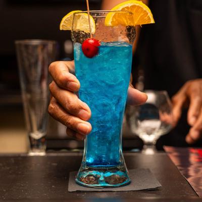 Hand holding a cocktail in pilsner glass, garnished with citrus slices and a cherry.