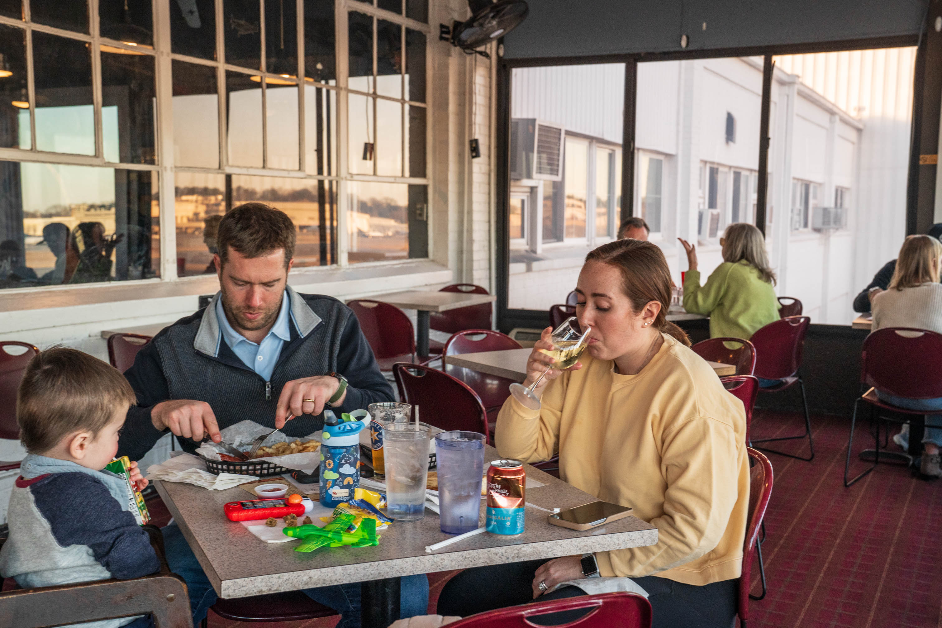 Patrons seated at tables next to large windows overlooking an airport runway