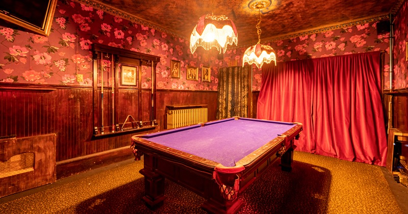A room with a pool table, red curtain on the wall and beautiful chandeliers