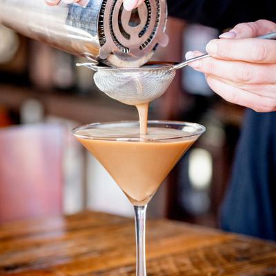 Bartender pouring an espresso martini into a martini glass.