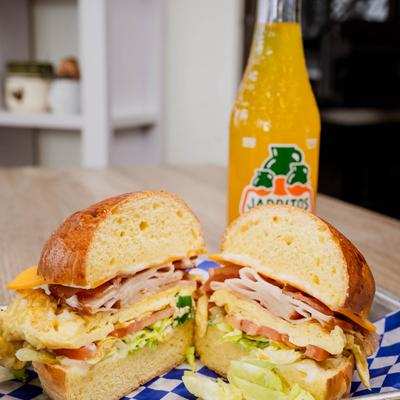 A halved breakfast sandwich with turkey, egg, and lettuce beside a soda.