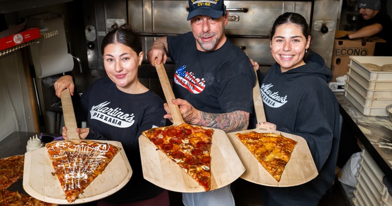 The main pizza master and helpers hold the pizzas on wooden shovels