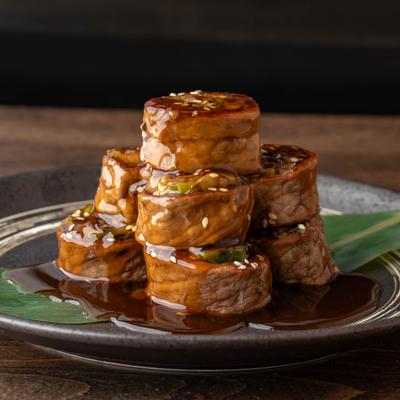Stacked beef rolls with teriyaki glaze and sesame seeds.