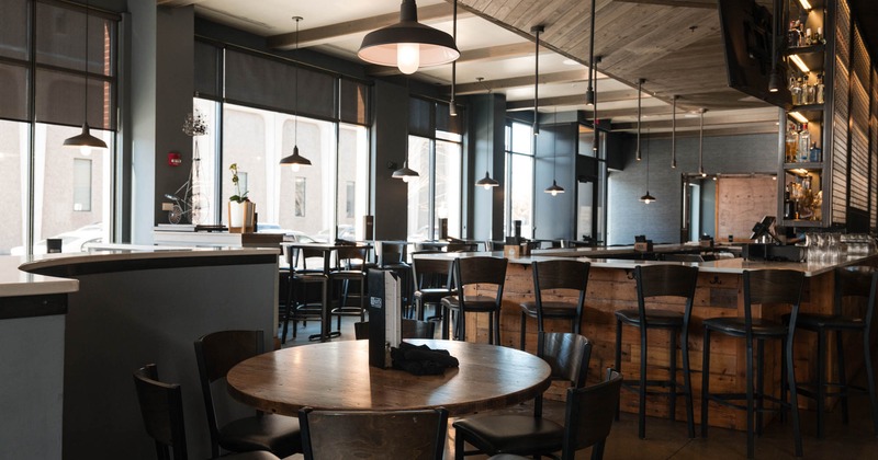 Interior, round wooden dining table, bar with bar stools in the back