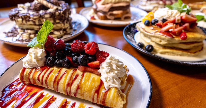Gourmet berry crepe plate surrounded by decadent pancake stacks on a wooden table