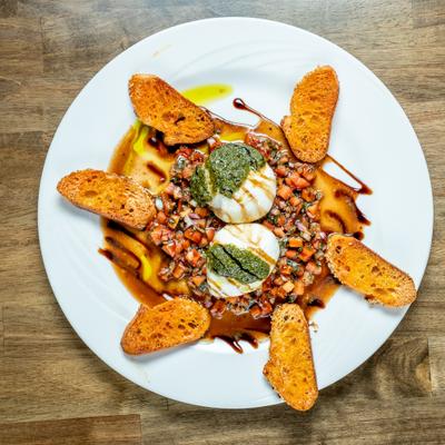 Bruschetta featuring burrata topped with a pesto, bruschetta mix and toasted crostini.