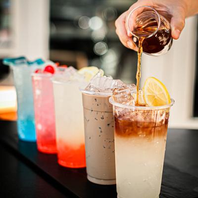 Lined up cups of assorted iced beverages with bartender's hand pouring one of the drinks