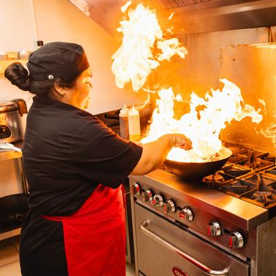 Cook preparing food over tall stove flames.