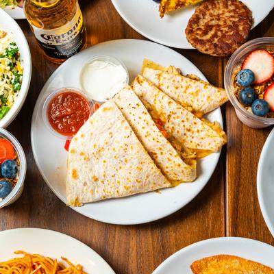 Chicken quesadilla with salsa and sour cream, served alongside assorted breakfast and brunch dishes.