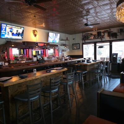 Spacious bar interior with wooden tables, high stools, and glowing back bar.