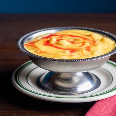 Silver dessert cup filled with Mango Fruity sits on a white plate atop a wooden table.