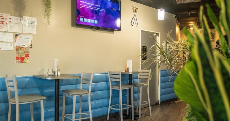 Tables with bar stools next to a wall with a large TV screen