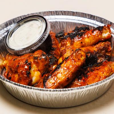 Glazed chicken wings served in a foil tin with a side cup of sauce.