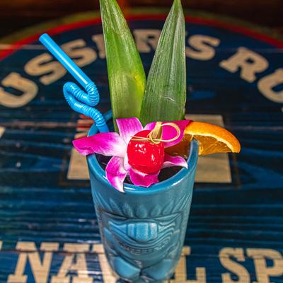 Rabbit Hole cocktail with pineapple leaves, orchid flower, and fruit garnish.