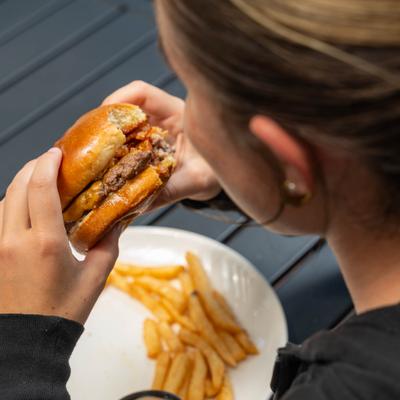 Person taking a bite out of a cheeseburger served with fries on a white plate.
