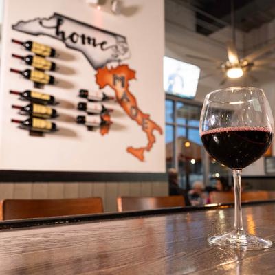 A glass of red wine resting on a bar counter, wall wine rack in the background.