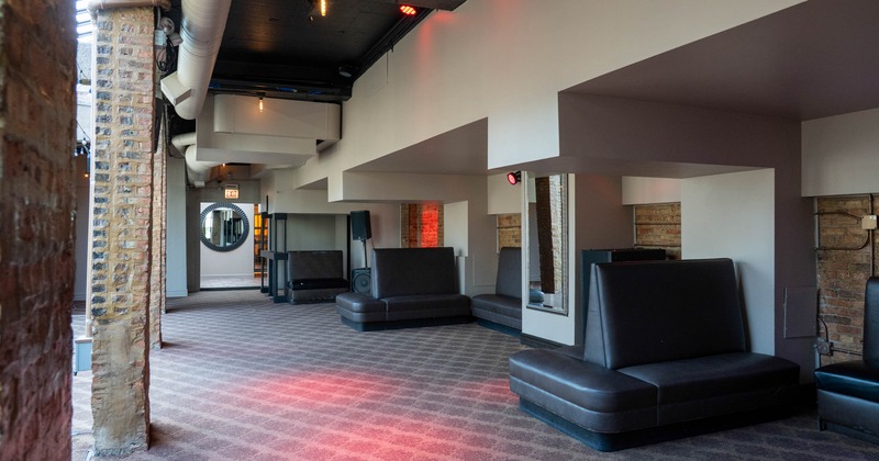 Interior of a lounge with patterned carpet, exposed brick walls, high-back leather booths, and industrial ceiling