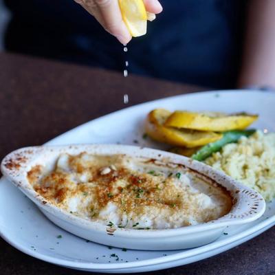 Hand squeezing a lemon wedge over the dish of baked scallops.