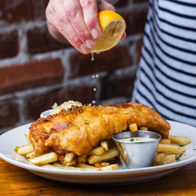A person squeezes lemon on fish and chips.