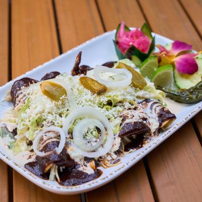 Mole enchiladas topped with diced onions, queso fresco, and jalapenos.