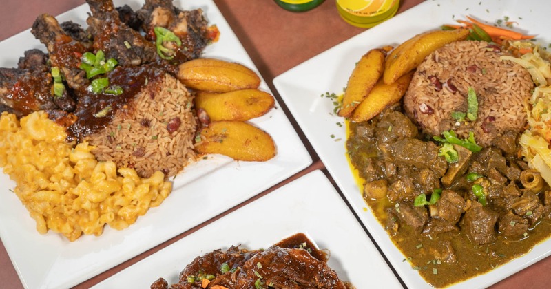 Plates of oxtails, wings, and curry goat accompanied with bottled beverages