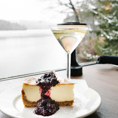 Homemade NY style cheesecake on a table by a window, accompanied with Lemon Twist Martini.