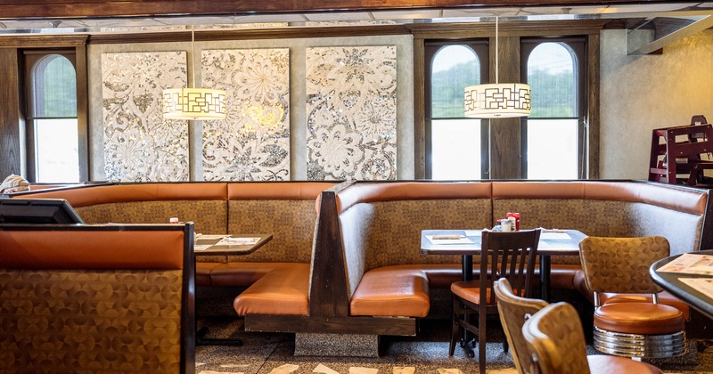 Interior - brown booths, a geometric light fixture, tables set with menus, floral wall decorations.