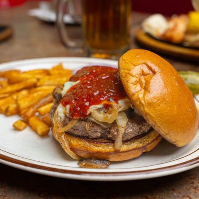 Burger topped with melted cheese, onions, and ketchup, served with fries.
