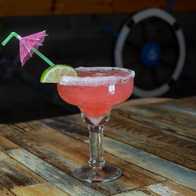 Salt rimmed margarita with a lime wedge and an umbrella on a wooden table.