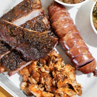 BBQ platter with pork ribs, smoked sausage, and pulled pork with sides.