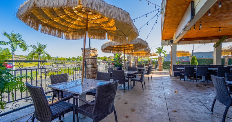 Outdoor restaurant patio with wicker furniture, tiki-style umbrellas, string lights