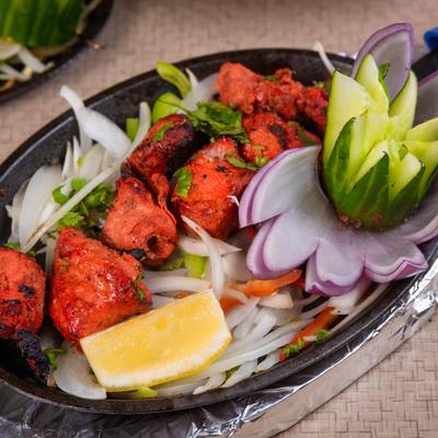 Chicken Tikka on a bed of sliced onions, served with a lemon wedge.