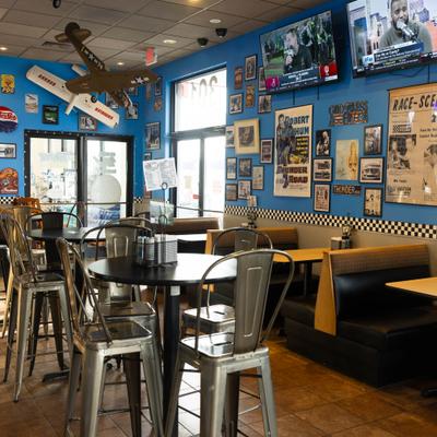 Interior of a diner with blue walls, retro decor, high-top tables, booths, and TVs.