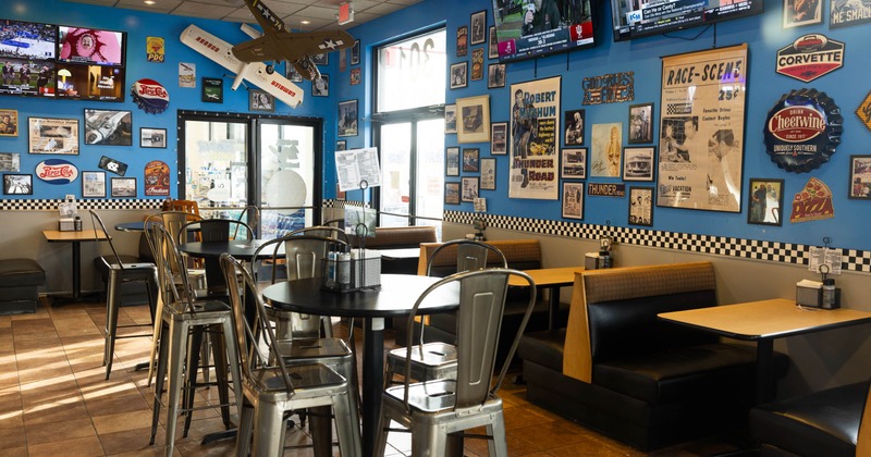 Interior of a diner with blue walls, retro decor, high-top tables, booths, and TVs