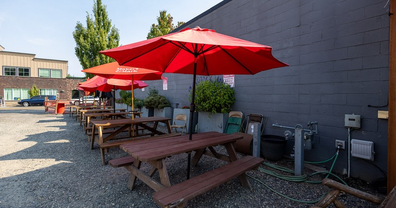 Outdoor seating area with wooden conjoined tables and benches and red parasols