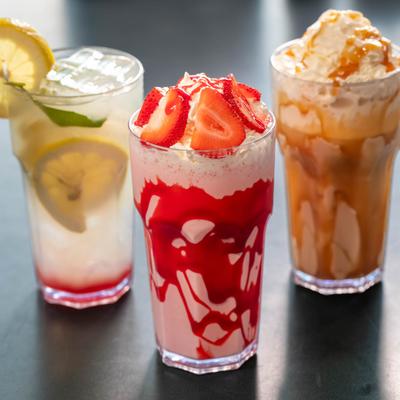 Lemonade, strawberry milkshake, and caramel milkshake on a dark surface.