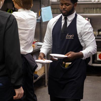 Server in a professional kitchen holding small plates of food.